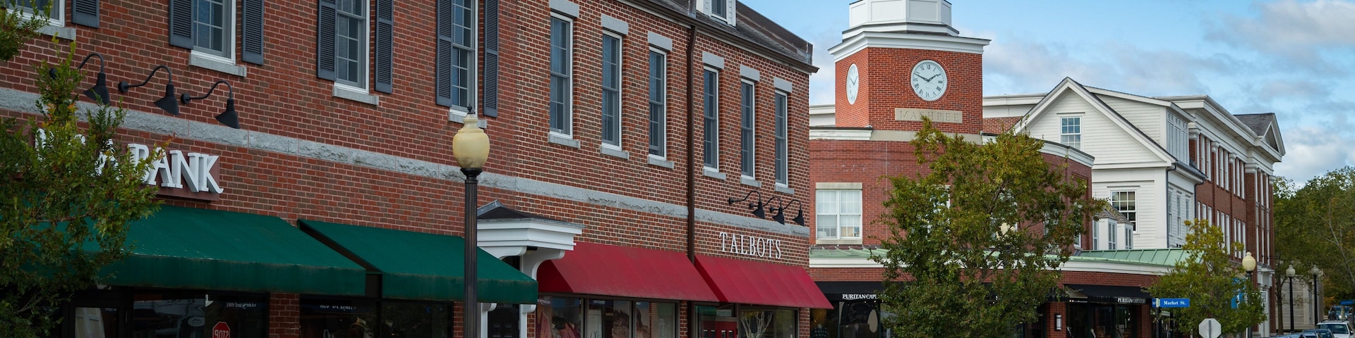 A street with brick buildings, a clock tower, and parked cars.