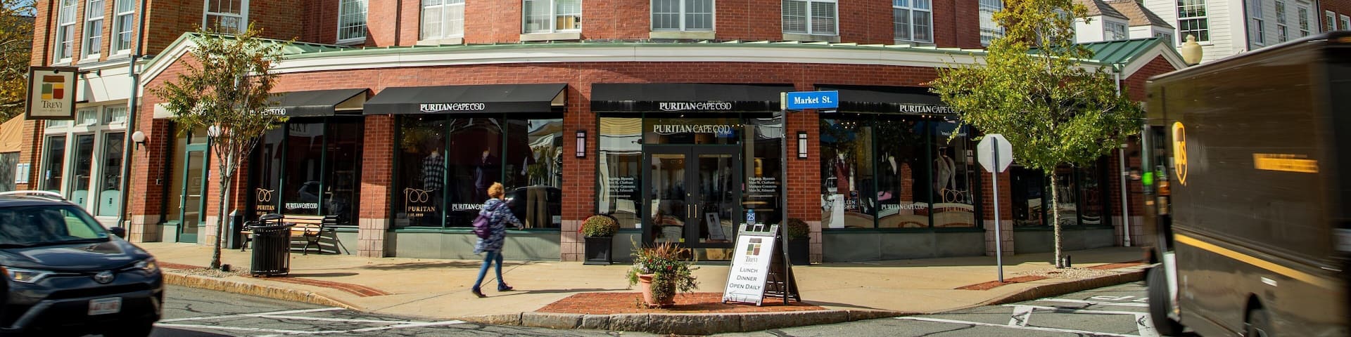 A historic building with a clock tower, named "MASHPIEE," and a sign for "PURITAN CAPE COD."