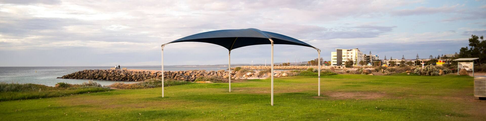 Blue shade sail on green lawn at beach foreshore with ocean view, Geraldton, Western Australia, 28 February 2023