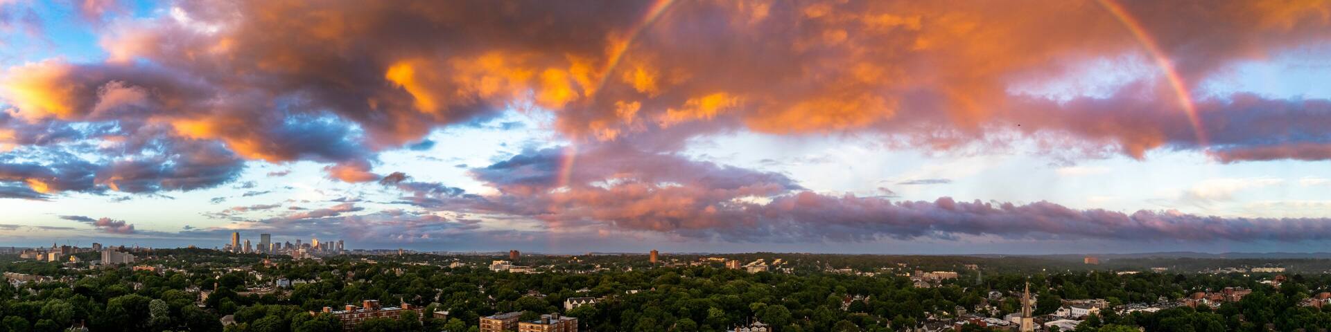 Aerial view of a picturesque cityscape with a vibrant rainbow over the skyline during sunset, Boston, Massachusetts, United States.