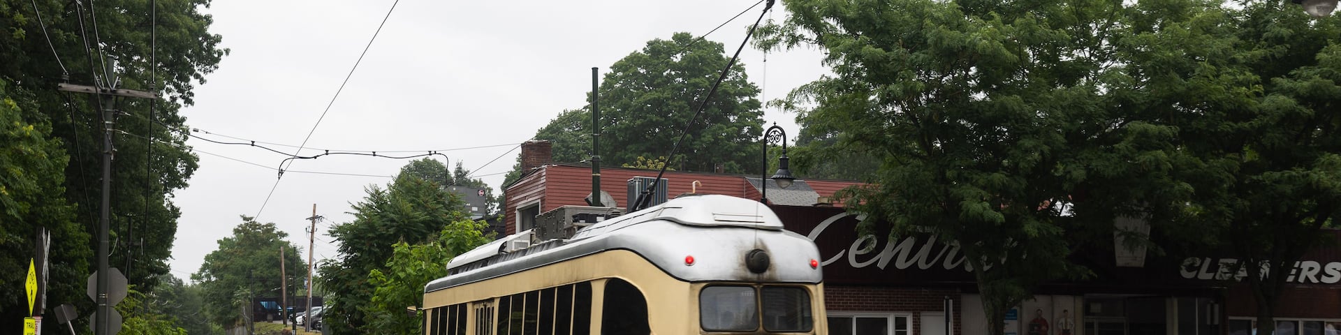 A vintage tram on tracks, a yellow and white train station platform, and a building with a sign that reads 'CLEANERS'.
