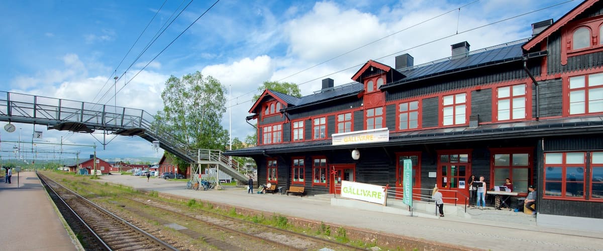 A train station with a red and black building, a pedestrian bridge, and multiple tracks.
