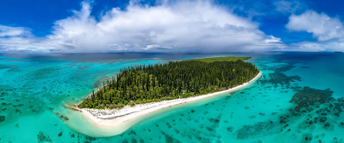 An aerial view of a tropical island with a white sandy beach, dense green forest, and clear turquoise waters.
