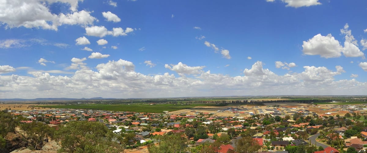A town with red-roofed houses, green fields, and a clear blue sky with clouds.