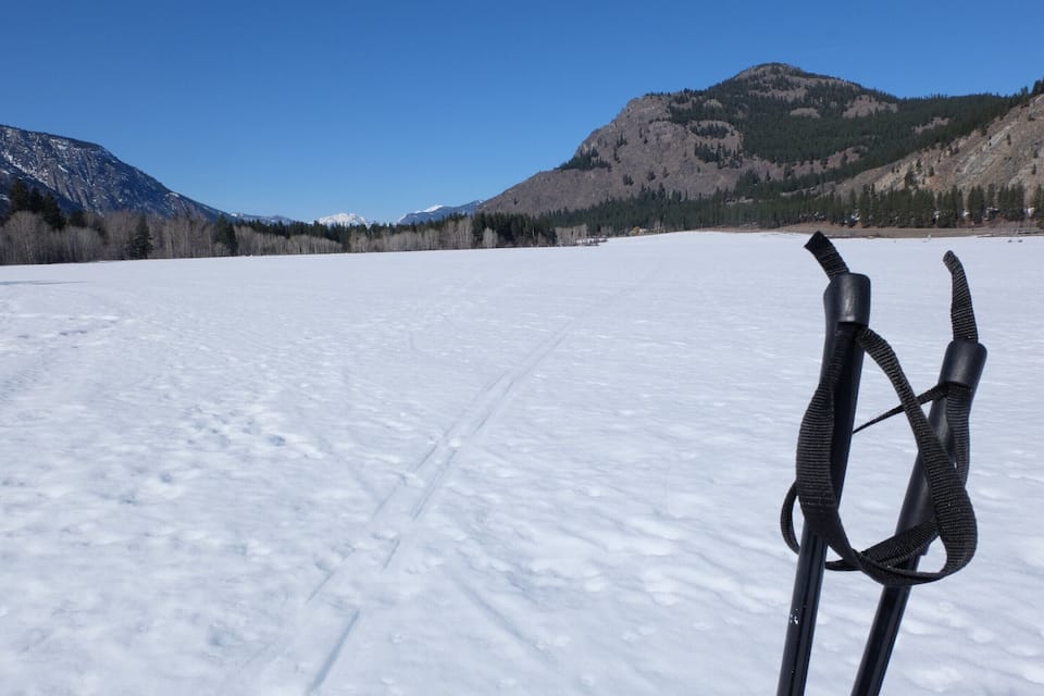 Paisaje nevado con una montaña al fondo y un par de esquíes en primer plano.