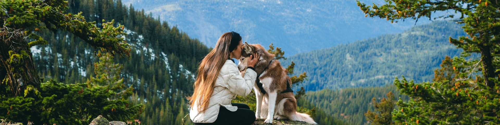 Uma mulher e um cão numa rocha com uma cordilheira ao fundo.