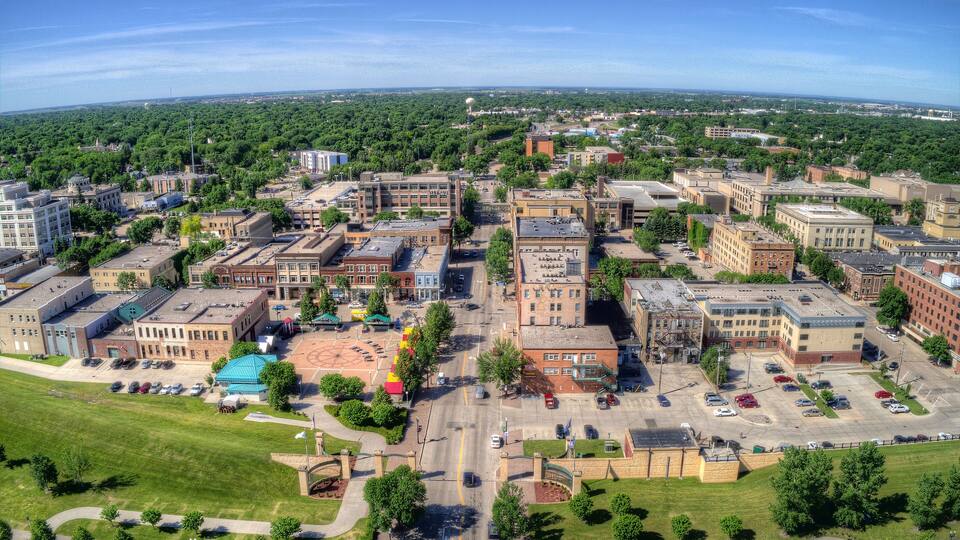 An aerial view of a city with a mix of historic and modern buildings, a large parking lot, and surrounding greenery.