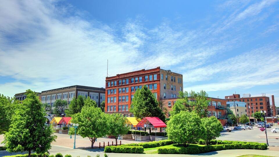 A cityscape with a prominent red building, green trees, and a clear blue sky.