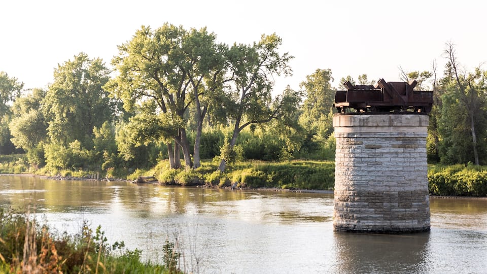 A stone pier extending into a calm river, surrounded by lush greenery and trees.