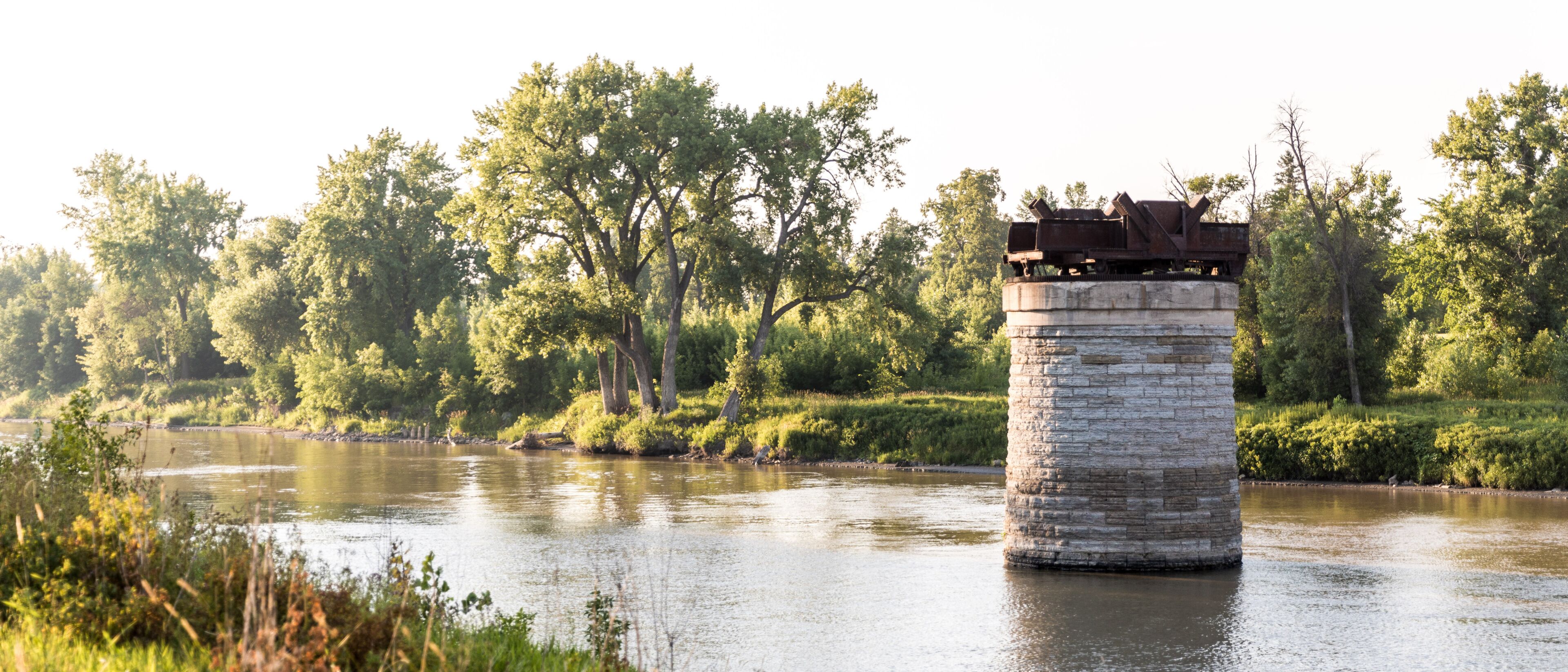 A stone pier extending into a calm river, surrounded by lush greenery and trees.