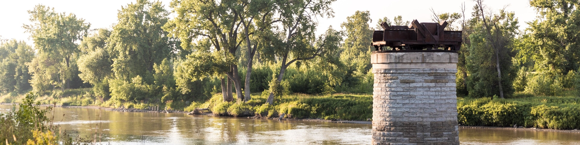 A stone pier extending into a calm river, surrounded by lush greenery and trees.