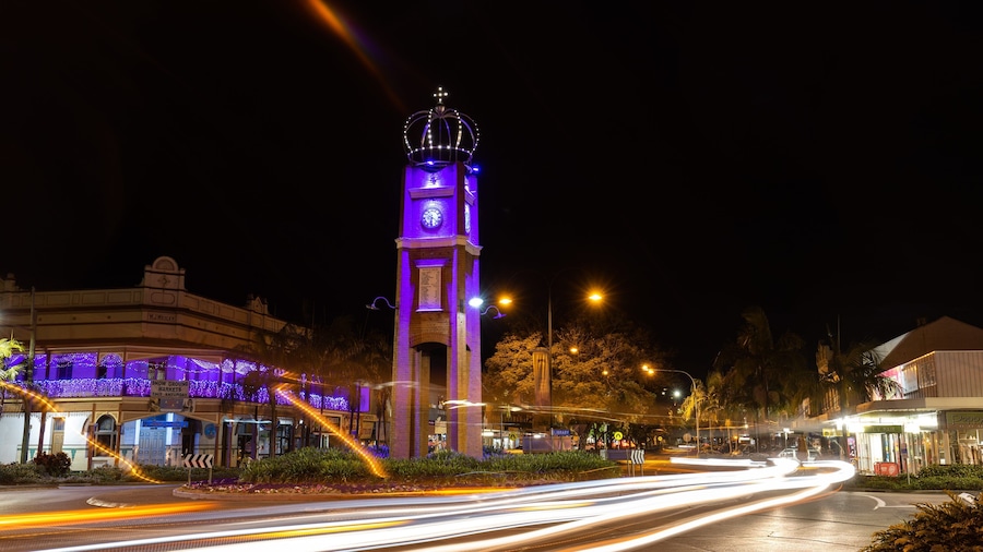 A brightly lit clock tower with a crown on top, surrounded by illuminated buildings and a busy street with light trails.