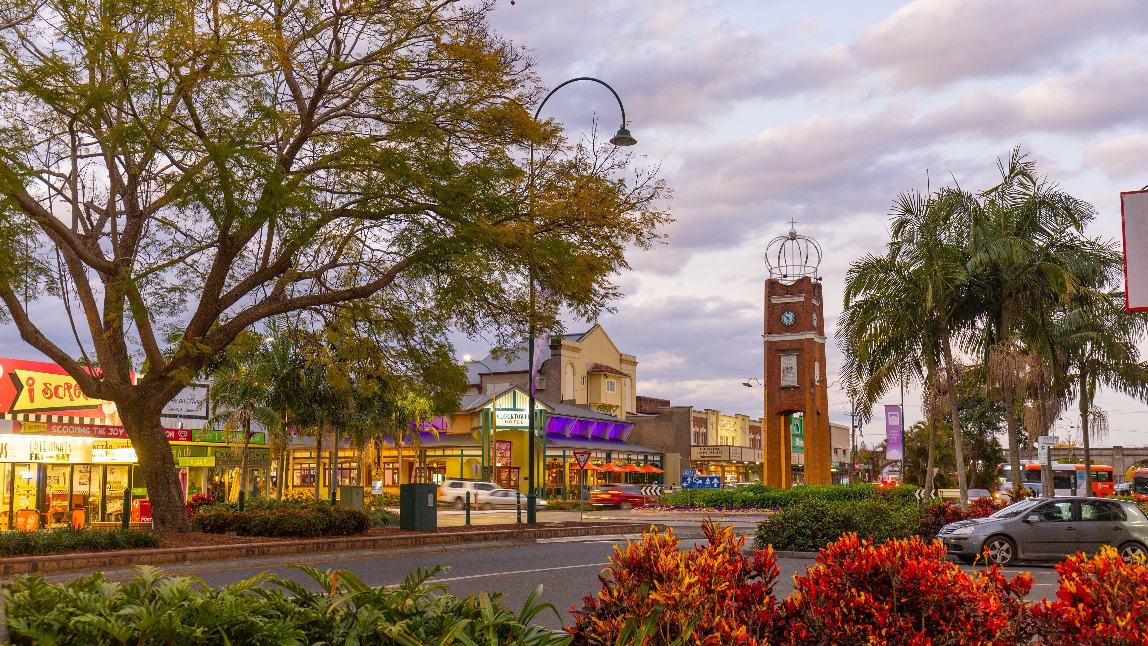 A street with a clock tower, shops, and palm trees.