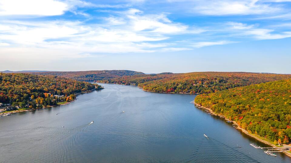 A river winding through a forested valley with boats on the water and houses along the shore.