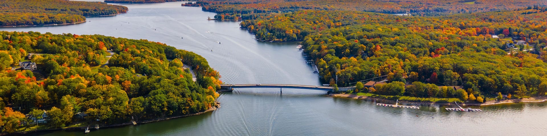A river with a bridge, surrounded by autumn-colored trees and a clear sky.