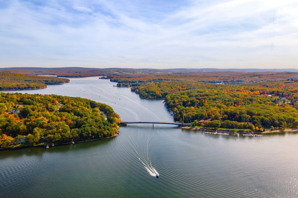 A river with a bridge, surrounded by autumn-colored trees and a clear sky.