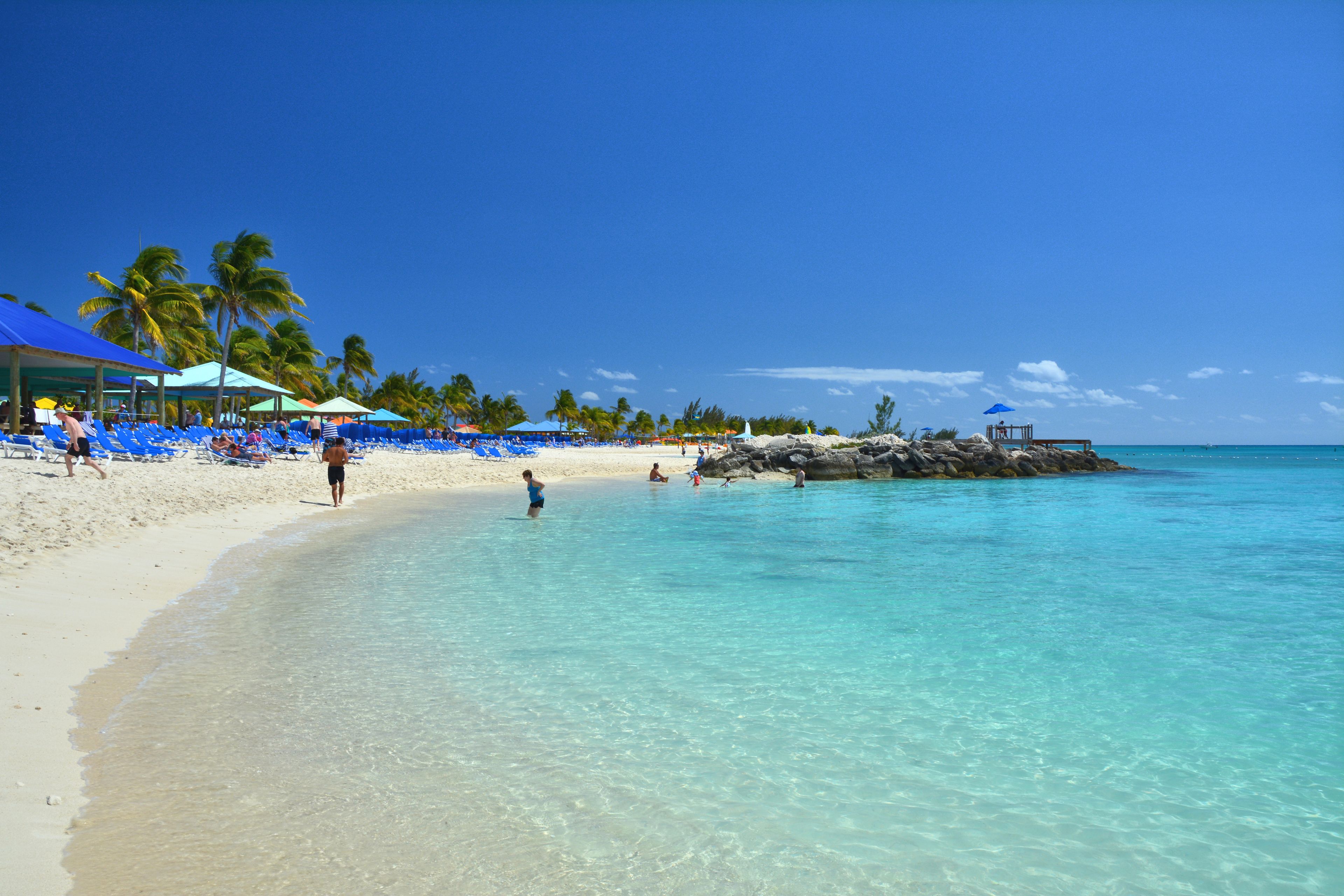 A beach with clear turquoise water, white sand, and palm trees.
