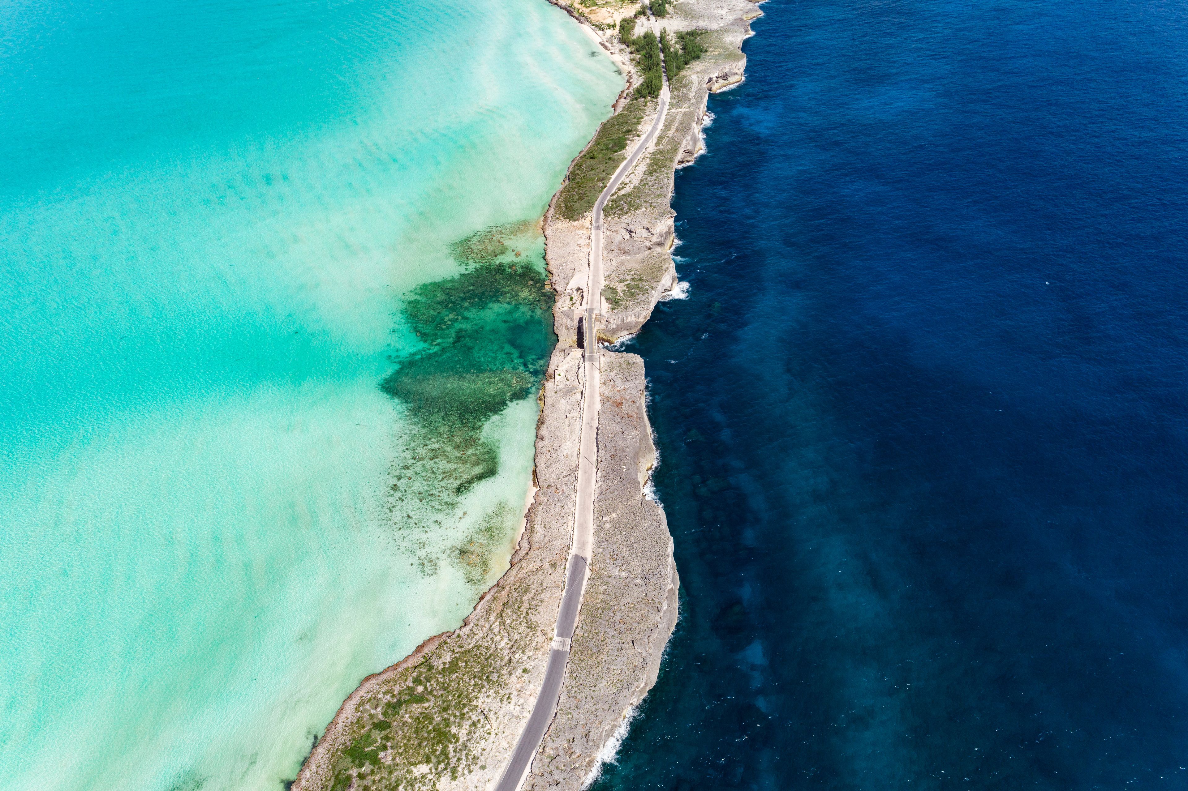 An aerial view of a coastal road with clear turquoise waters and a rocky shoreline.