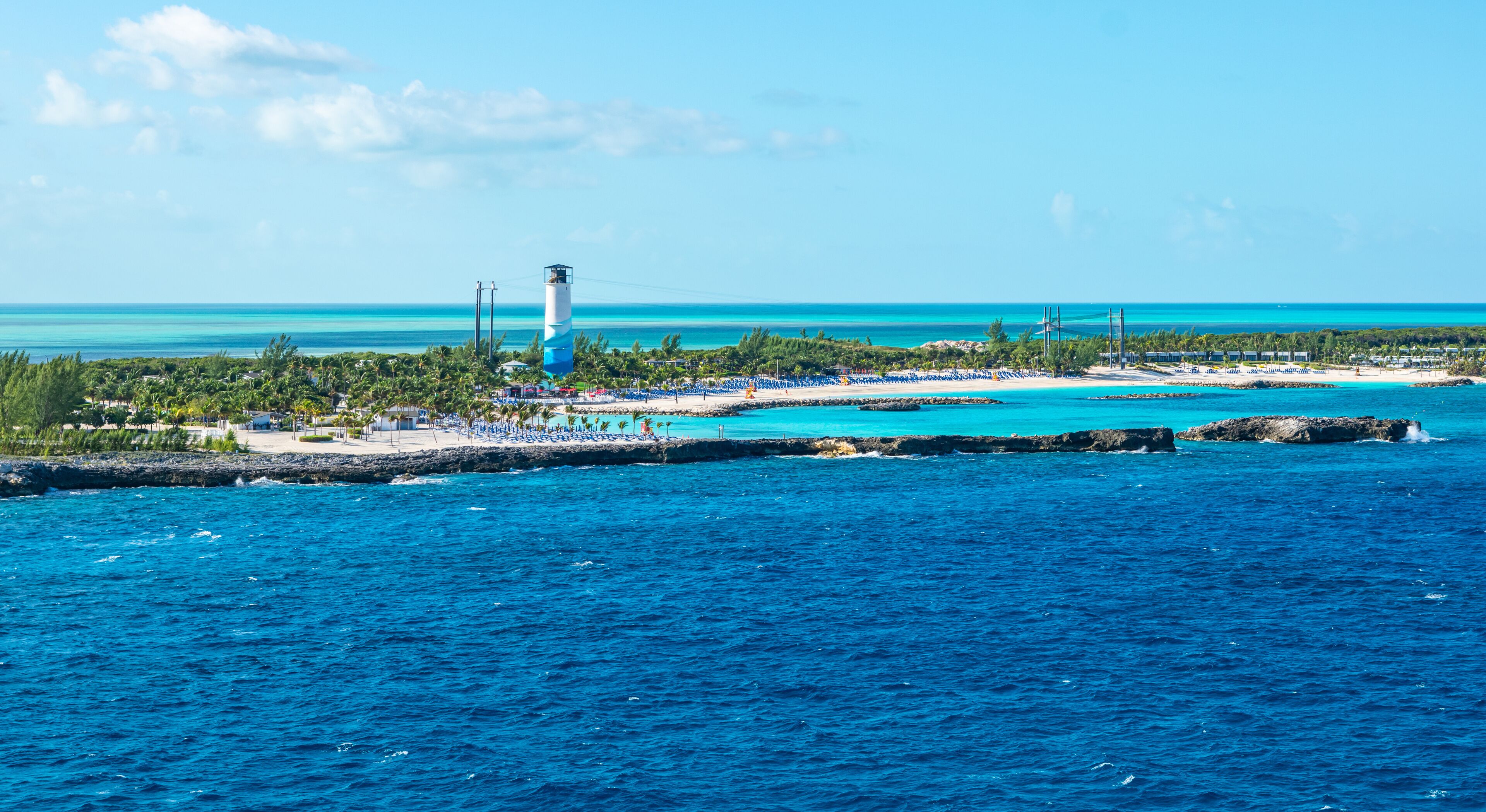 A coastal resort with a lighthouse, turquoise waters, and a sandy beach.