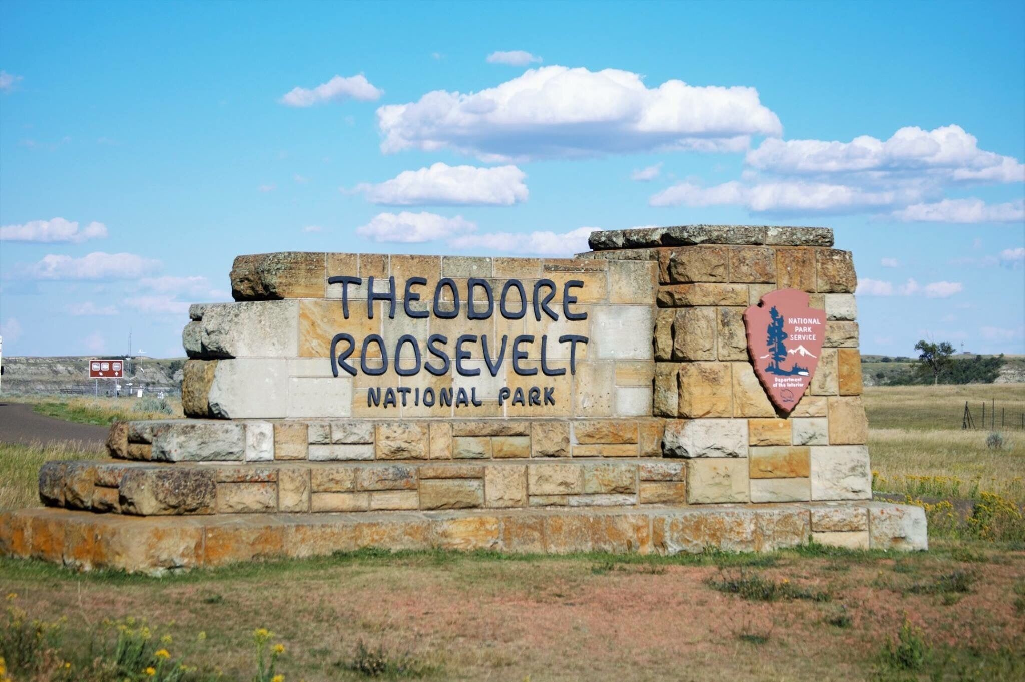 A stone sign for Theodore Roosevelt National Park with a National Park Service emblem.
