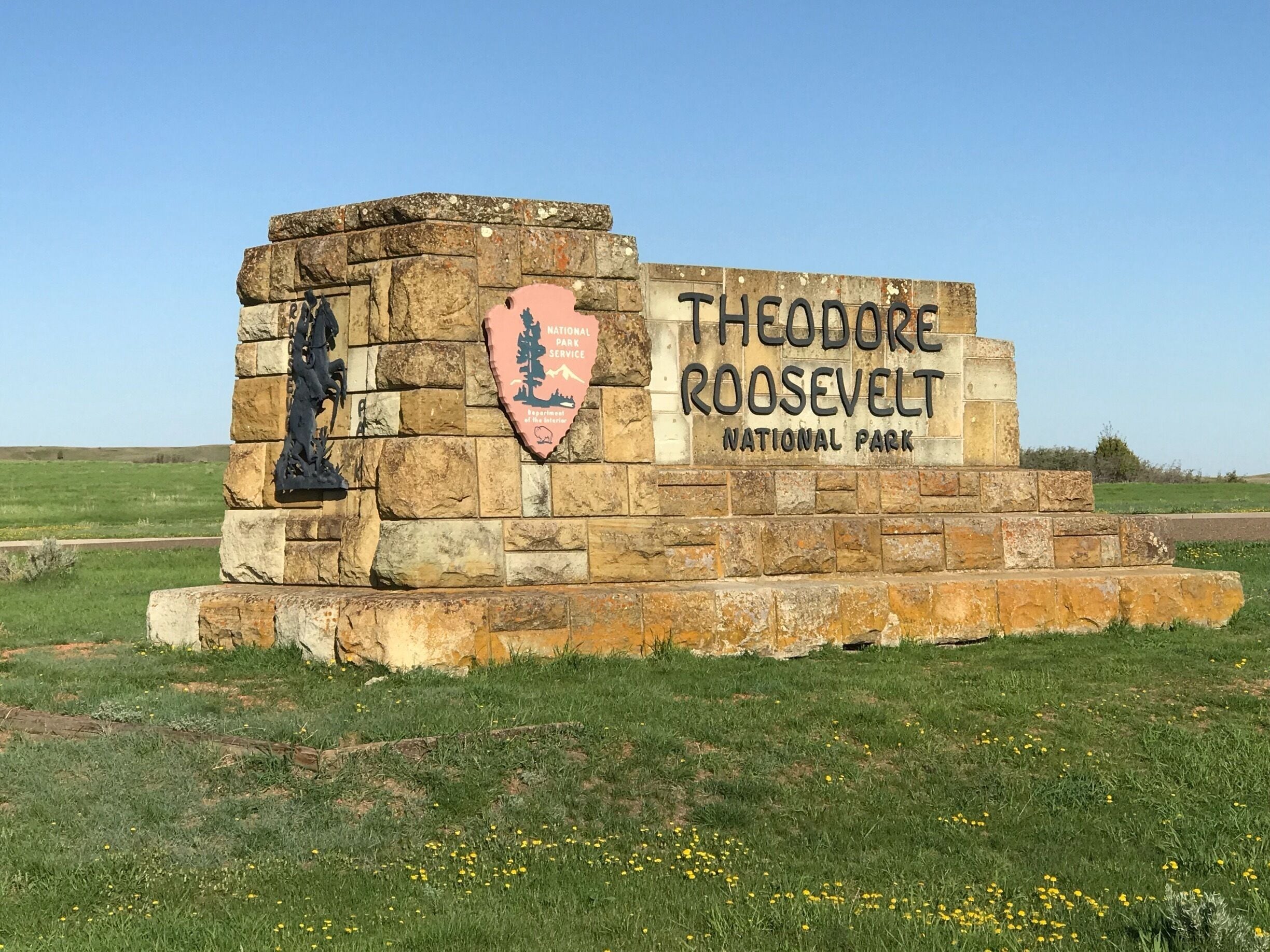 A stone monument with a silhouette of Theodore Roosevelt and a pink shield with trees and mountains.