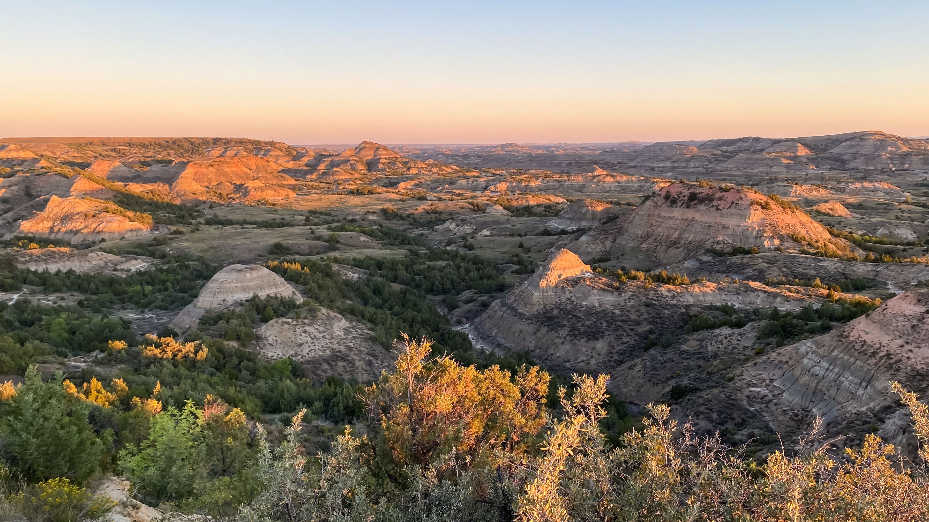 Un extenso paisaje de tierras baldías escarpadas con destacadas formaciones de hoodoos y vegetación dispersa.