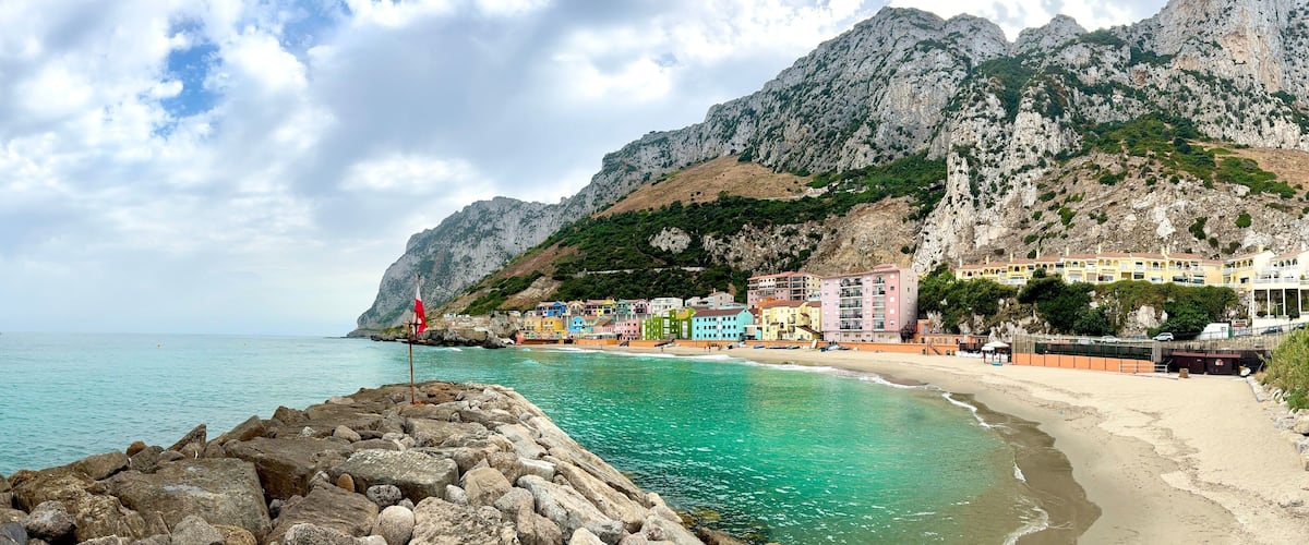 A coastal town with colorful buildings, a rocky shoreline, and a mountainous backdrop.