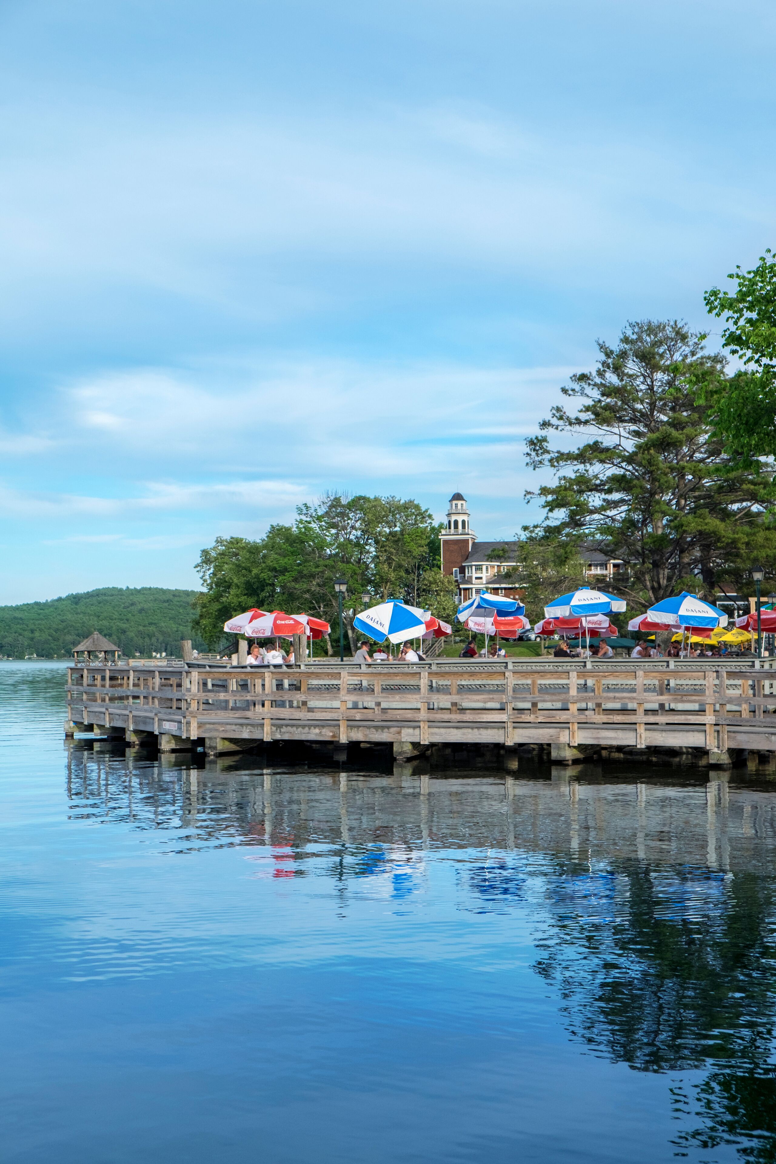 A wooden pier extending into calm water, with several colorful umbrellas and people seated.