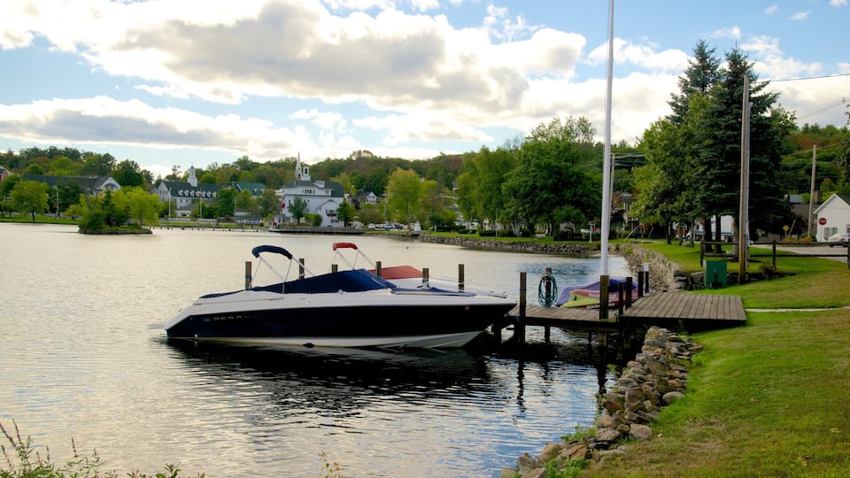 A speedboat docked at a pier with a lake, trees, and houses in the background.