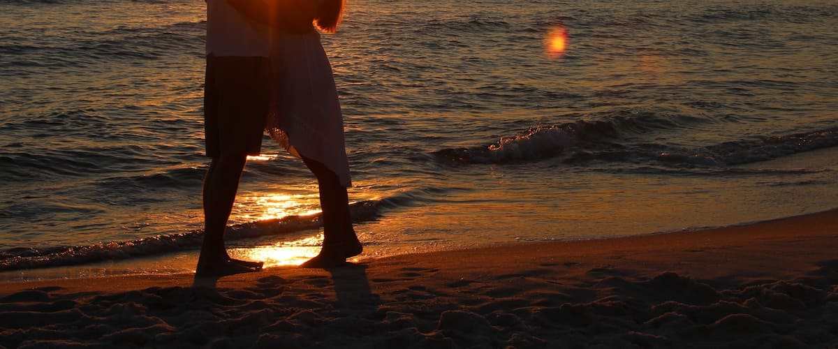 A couple embracing on a beach at sunset with the sun setting over the ocean.