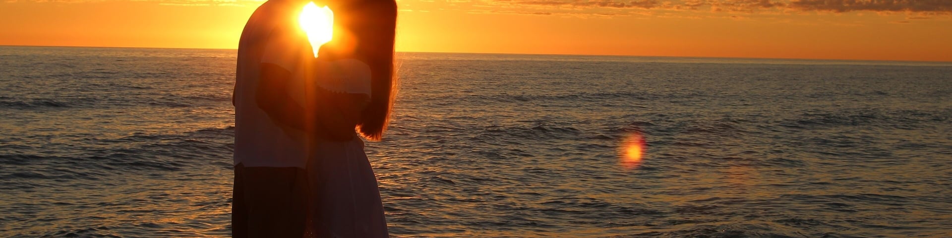 A couple embracing on a beach at sunset with the sun setting over the ocean.