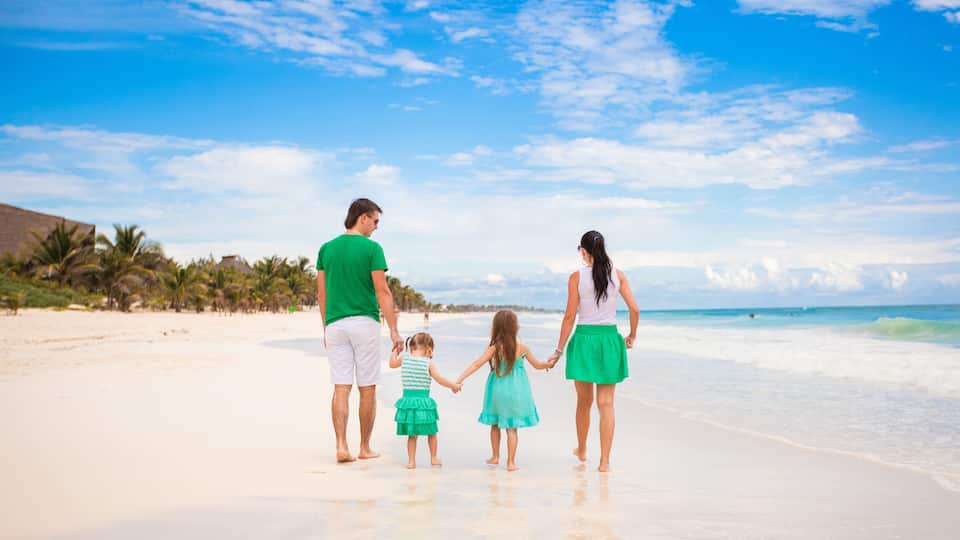 A family on a sandy beach with palm trees and ocean waves in the background.