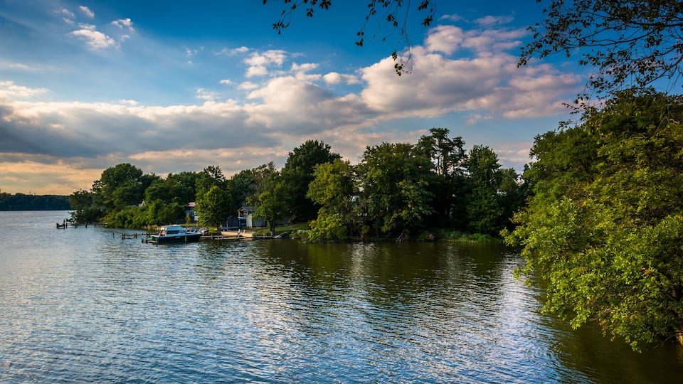 A calm lake with a boat docked on the left, surrounded by lush greenery and trees.