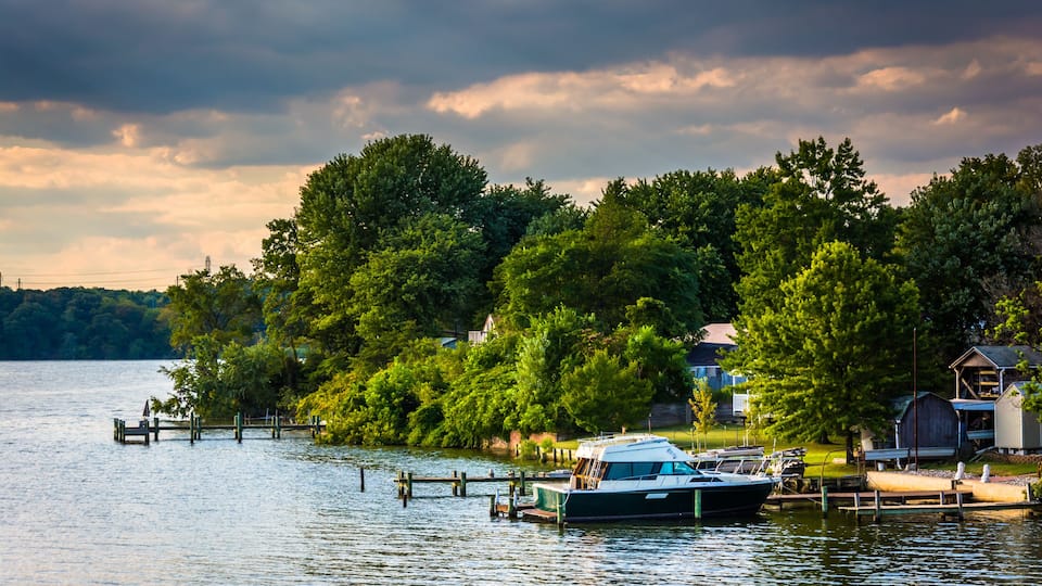 A lake with a dock, a boat, and houses surrounded by trees.