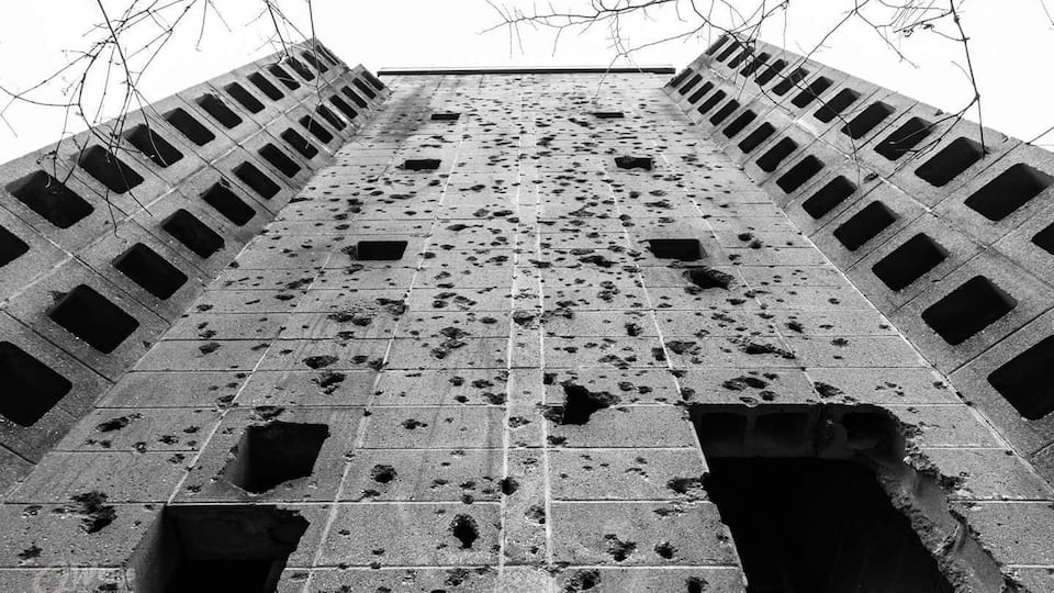 A tall, deteriorating concrete structure with multiple square openings and scattered debris.