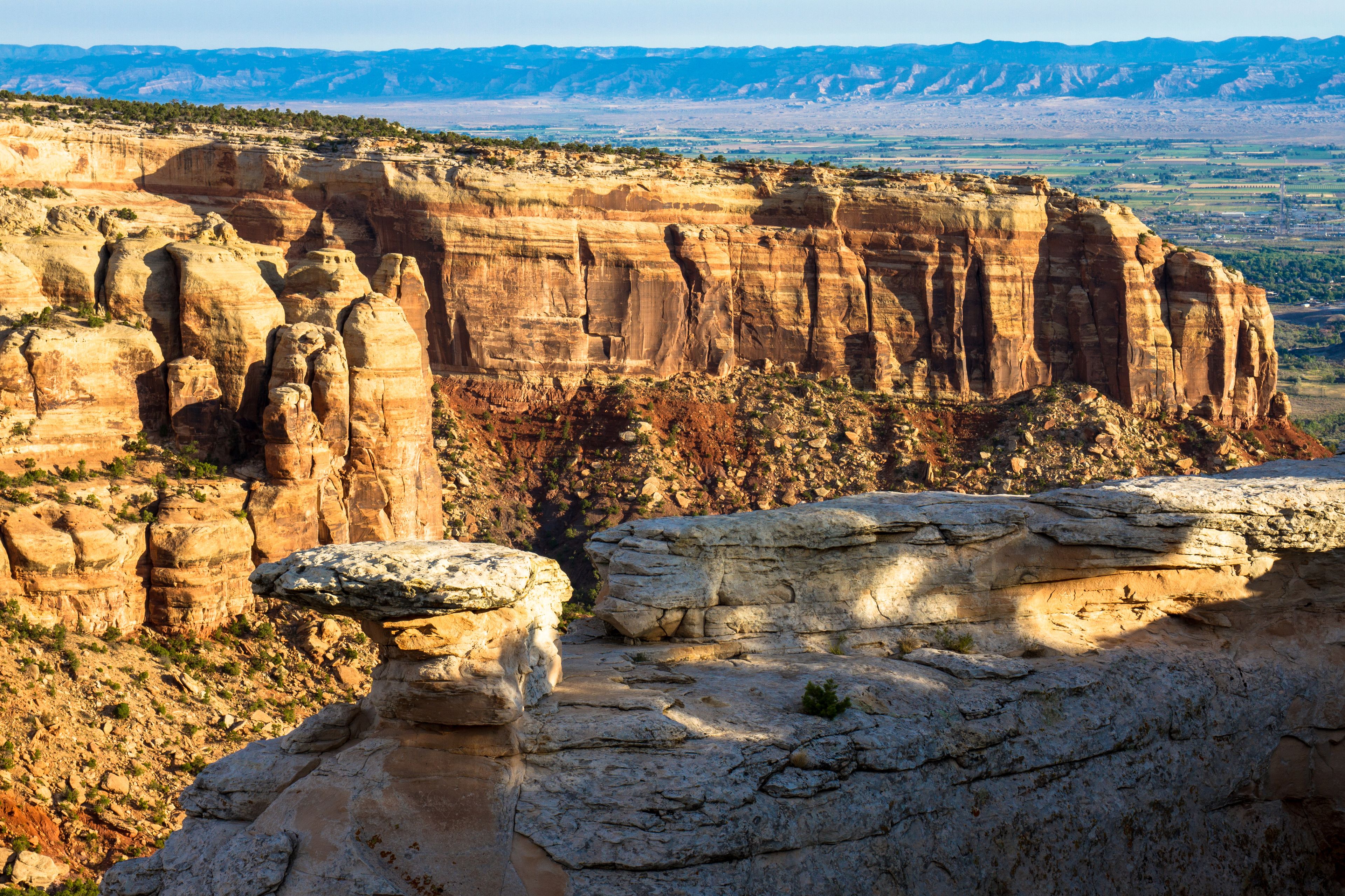 A rugged canyon landscape with layered rock formations and sparse vegetation.