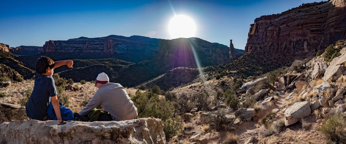 Two people sitting on a rock with a canyon and a prominent rock formation in the background.