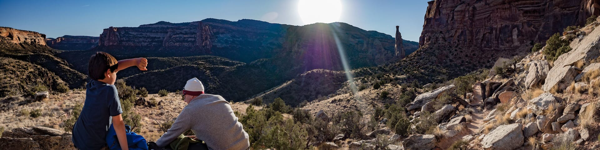 Two people sitting on a rock with a canyon and a prominent rock formation in the background.