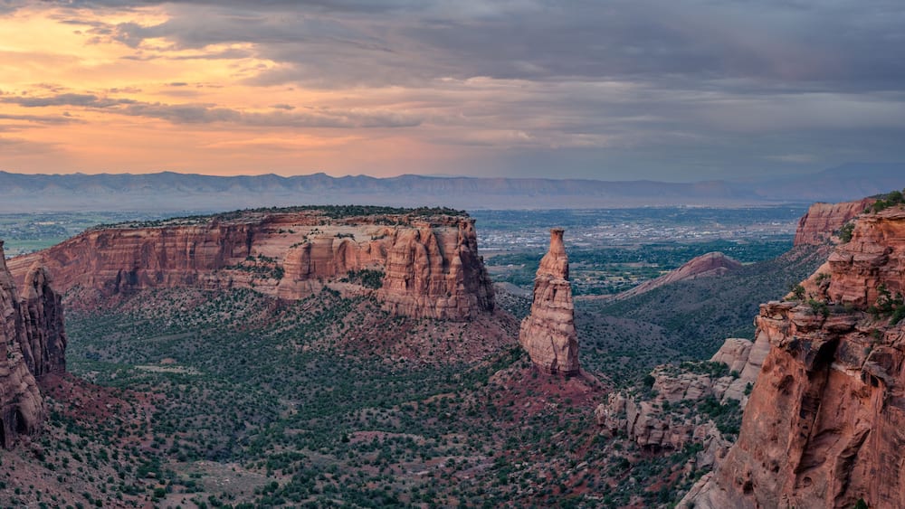 A canyon landscape with prominent red rock formations and a distant mountain range.