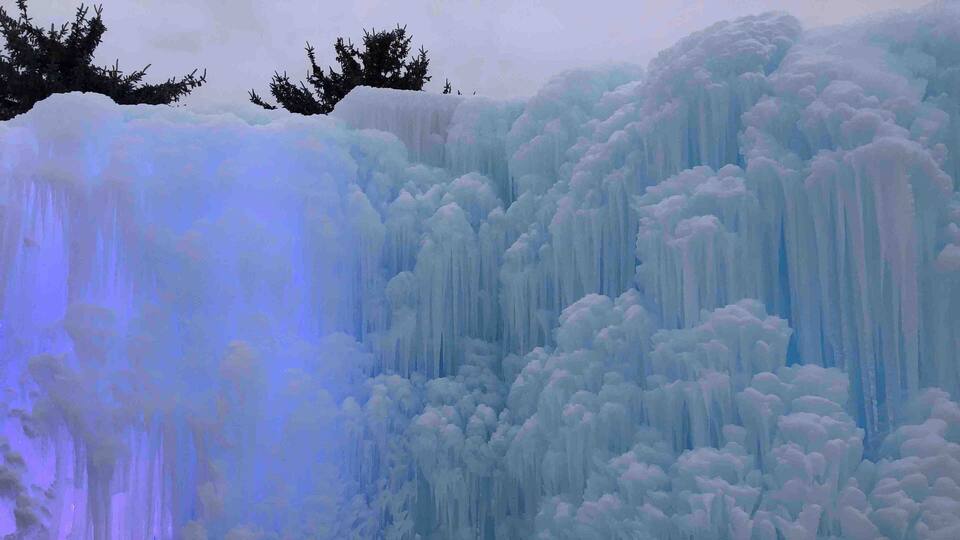 A large, illuminated ice waterfall with surrounding snow-covered trees.
