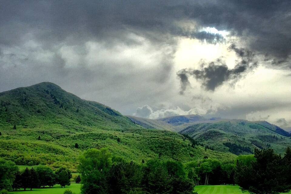 A lush green golf course with rolling hills and a cloudy sky.