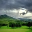 Un magnifique terrain de golf verdoyant, avec des collines ondoyantes et un ciel nuageux.