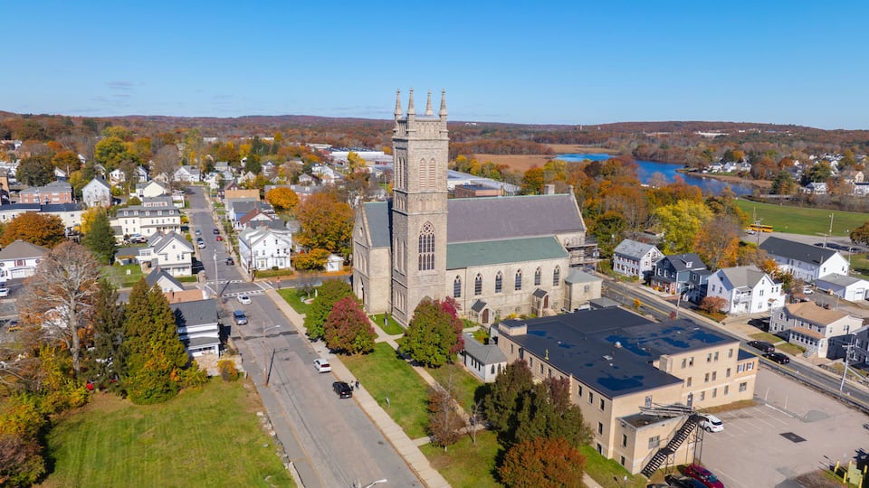 A church with a tall steeple, surrounded by residential houses and a parking lot.