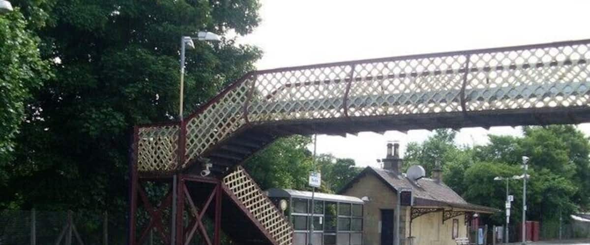 A railway station with a covered pedestrian bridge, tracks, and a platform.