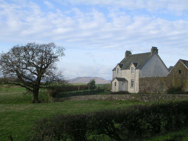 A rural house with a large tree in the foreground and a fence in the background.