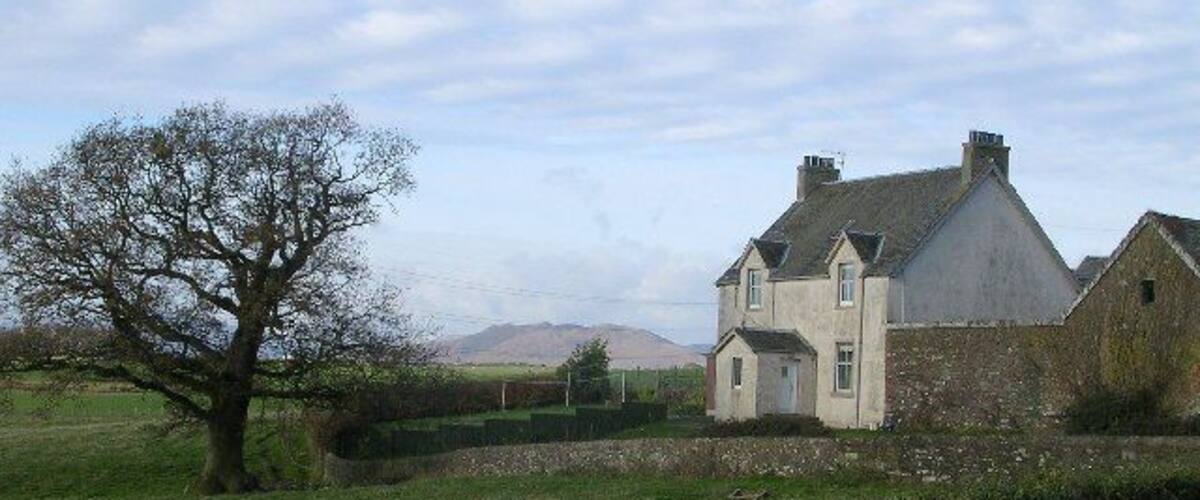 A rural house with a large tree in the foreground and a fence in the background.