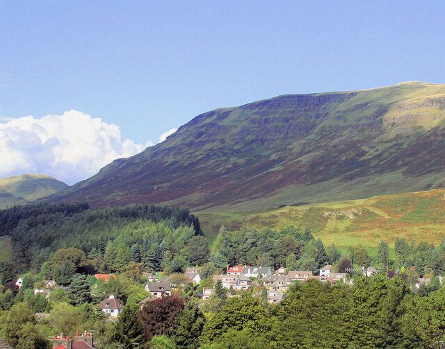 A village nestled in a valley with rolling hills and dense forests in the background.