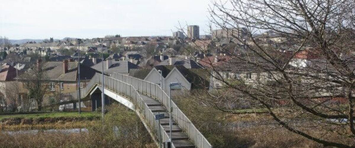 A pedestrian bridge over a river, surrounded by green grass and a pathway.