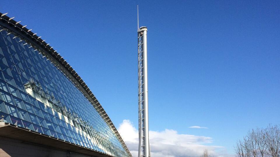 A modern building with a glass facade and a tall, slender tower.