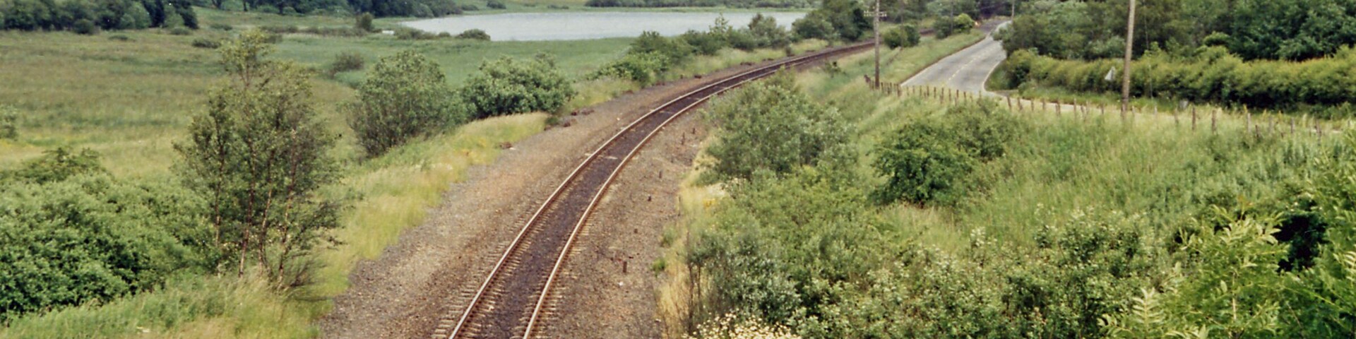 Site of Caldwell - later Uplawmoor, station. This is the former Glasgow, Barrhead & Kilmarnock (later Glasgow & South-Western) line from Glasgow St Enoch, later from Glasgow Central - and by 1986 single-track, to Kilmarnock and Carlisle. Until 2/4/62 Caldwell was named 'Uplawmoor'; it was closed on 7/11/66 - after having been portrayed on TV as 'Tannochbrae' in 'Dr Finlay's Casebook'. The water ahead is Loch Libo.